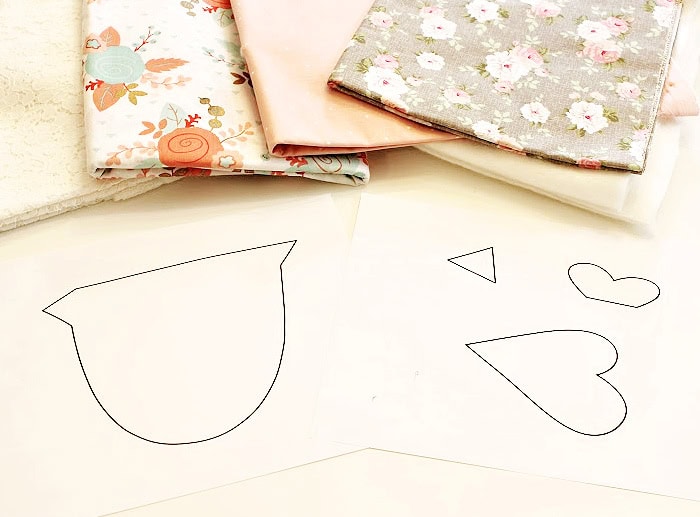 Fabric chicken pattern pieces, quilt batting, and fabric supplies arranged on a work surface before starting this DIY fabric chicken sewing project.
