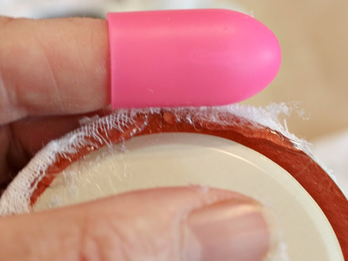 Folding a printed fabric circle around a padded mason jar lid insert while centering the image.