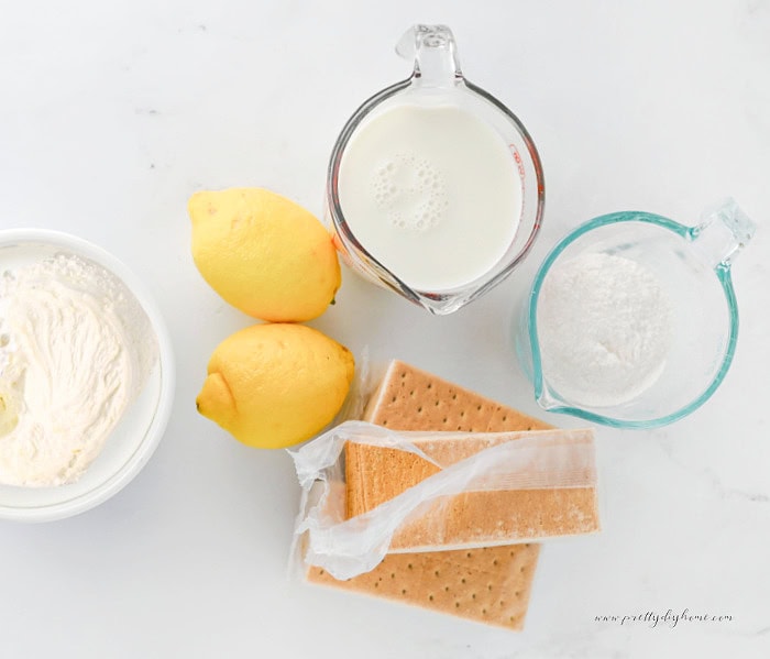 Ingredients for lemon icebox cake including whipped cream, lemons, graham crackers, and powdered sugar