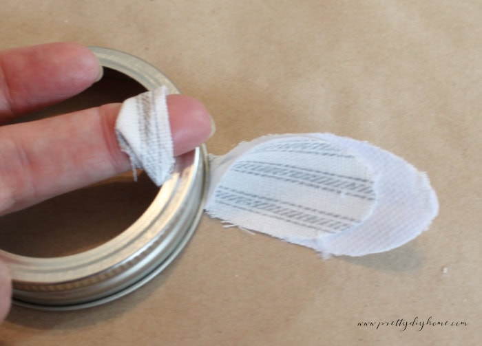 Folded fabric blossom positioned beneath a mason jar ring with the loop on one side and the fabric ends on the other.