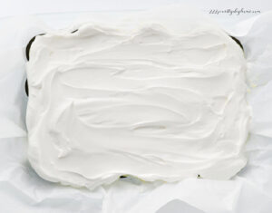 Whipped cream and cream cheese filling spread over Oreo cookies in a baking dish.