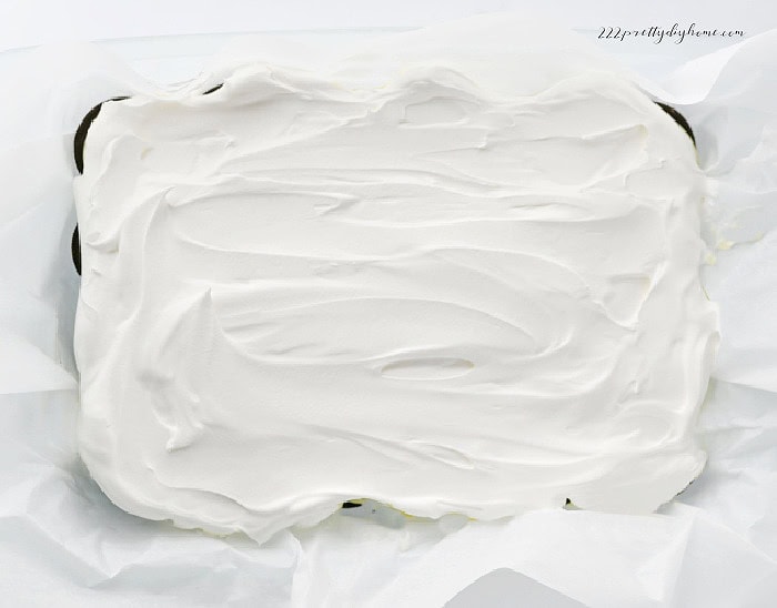 Whipped cream and cream cheese filling spread over Oreo cookies in a baking dish.