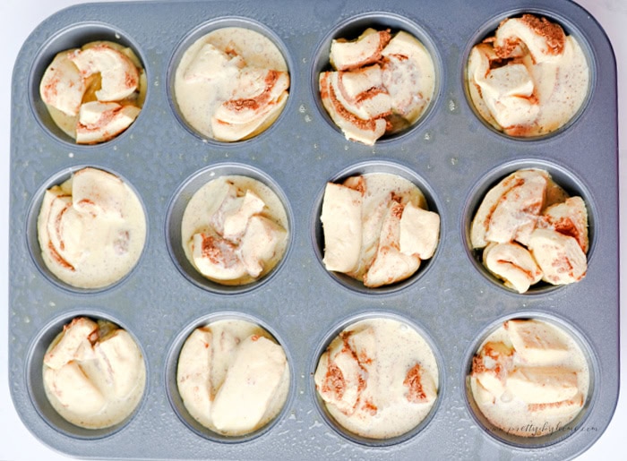 Custard mixture poured over cinnamon roll pieces in a muffin tin before baking.