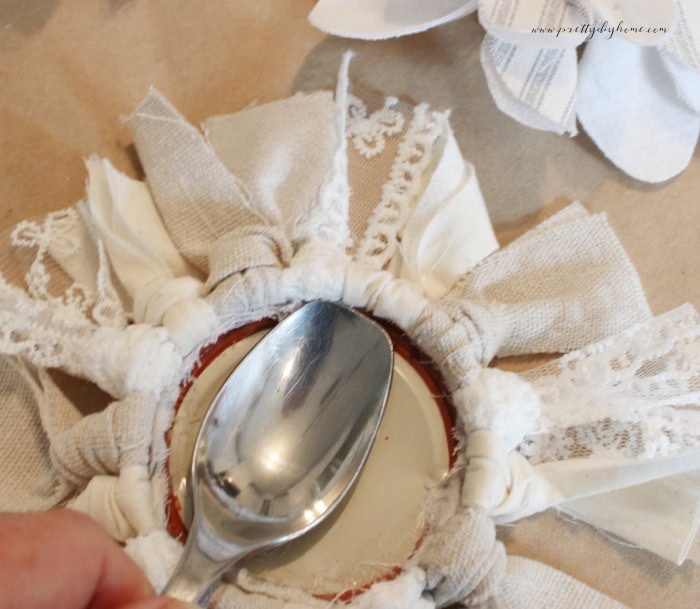 Using a spoon to press a padded fabric center into a DIY jar ring flower.