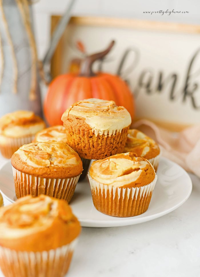 Pumpkin cheesecake muffins with cream cheese swirl arranged on a white plate.