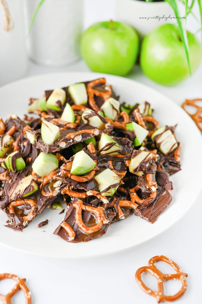 Caramel apple bark served on a plate with fresh Granny Smith apples and crunchy pretzels.