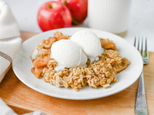 Slow cooker apple crisp served on a white plate with two scoops of vanilla ice cream, featuring tender cinnamon apples and a buttery oat crumble topping.