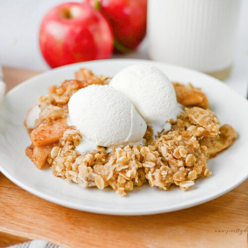Slow cooker apple crisp served on a white plate with two scoops of vanilla ice cream, featuring tender cinnamon apples and a buttery oat crumble topping.