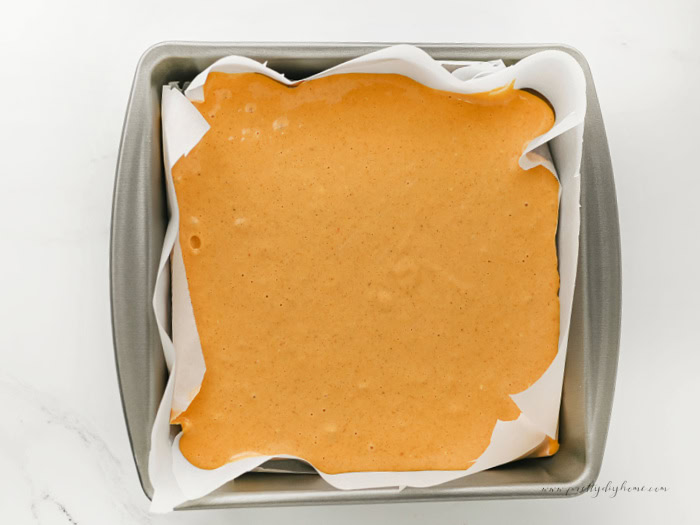 Pumpkin cream cheese filling spread evenly over brownie batter in a parchment lined square baking pan.