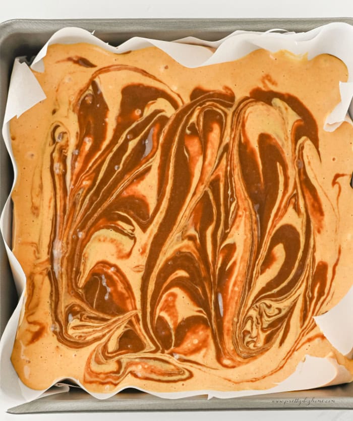 Pumpkin cream cheese filling swirled into chocolate brownie batter in a parchment lined square baking pan before baking.