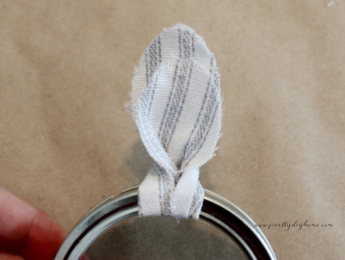 Fabric blossom being twisted into position on a mason jar ring before tightening the loop completely.