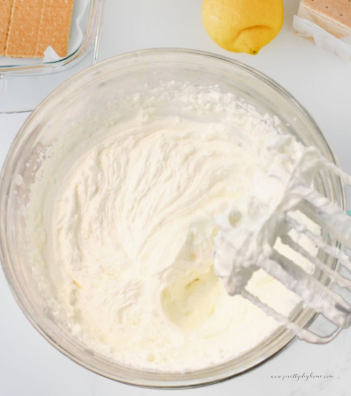Whipped cream being prepared for lemon icebox cake in a glass mixing bowl.