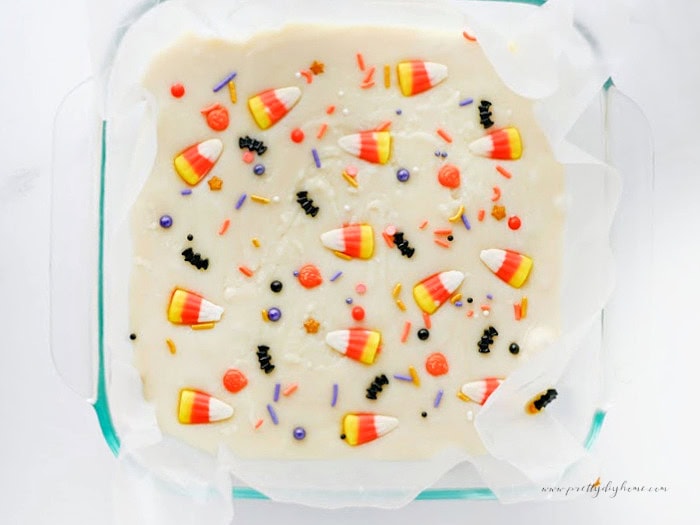 An overhead view of white chocolate Halloween fudge topped with candy corn and colourful Halloween sprinkles in a parchment-lined pan.