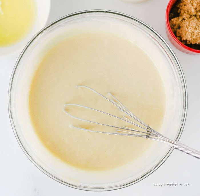 Cinnamon roll poke cake batter mixed until smooth in a clear glass bowl with a whisk.