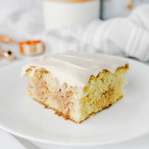 Close-up of a slice of cinnamon roll poke cake with soft vanilla cake, cinnamon brown sugar filling, and a thick layer of cream cheese frosting.