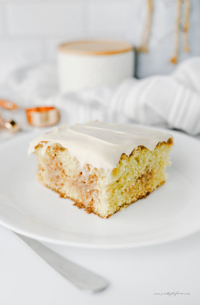 Close-up of a slice of cinnamon roll poke cake with soft vanilla cake, cinnamon brown sugar filling, and a thick layer of cream cheese frosting.