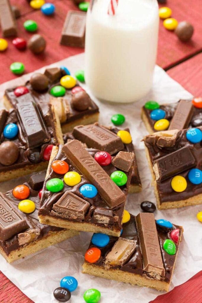 A stack of candy bar blondies topped with chocolate frosting, assorted candy bars, and colourful chocolate candies.