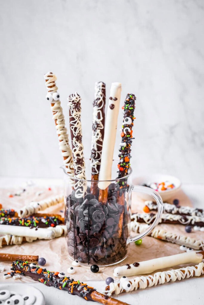Assorted chocolate covered pretzel rods are decorated as mummies, ghosts, and monsters with white chocolate drizzle, colourful sprinkles, chocolate chips, and candy eyes.
