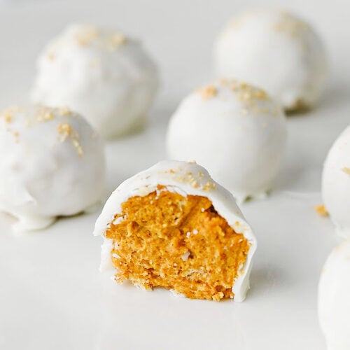 A plate of easy pumpkin truffles with one truffle split in half to reveal the creamy pumpkin filling beneath a smooth almond bark coating.