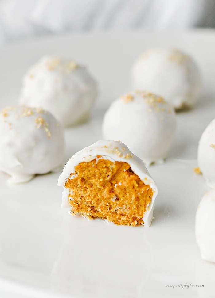 A plate of easy pumpkin truffles with one truffle split in half to reveal the creamy pumpkin filling beneath a smooth almond bark coating.
