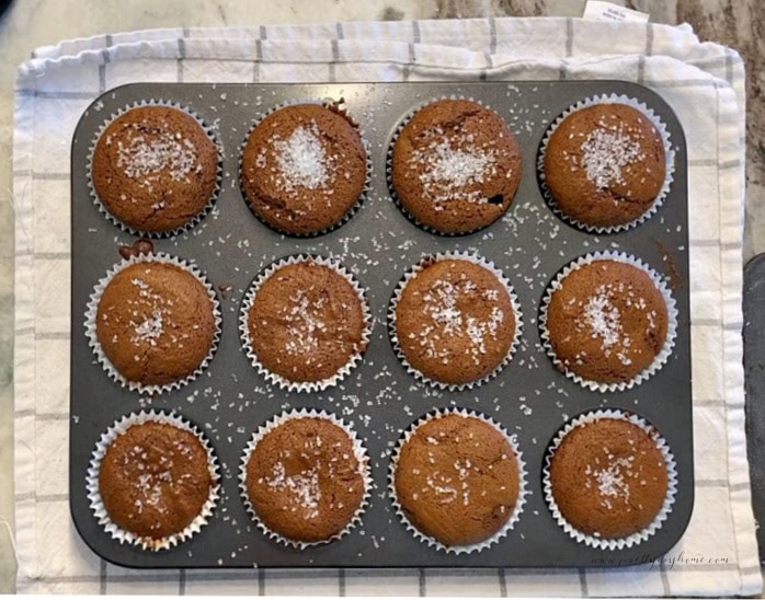 Twelve gingerbread muffins topped with sparkling sugar in a muffin tin.