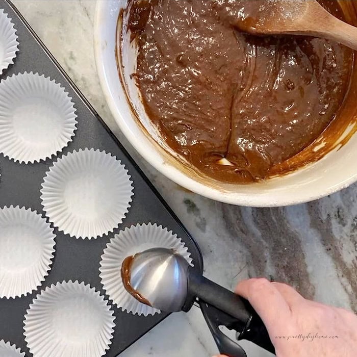 Gingerbread muffin batter being scooped into paper lined muffin cups.