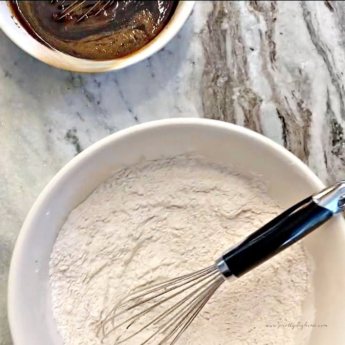 Dry ingredients for gingerbread muffins in a white bowl with the molasses mixture nearby.
