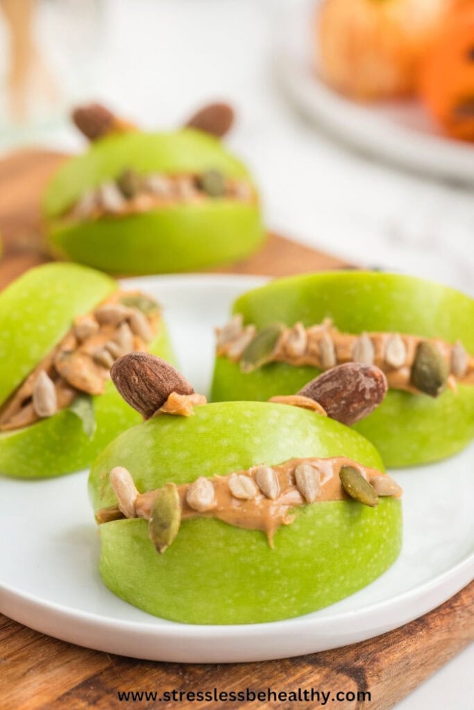 Green apple monster mouths filled with nut butter, seeds, and almond ears, served on a white plate.