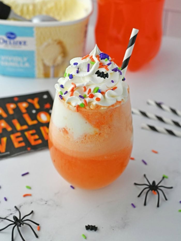 Orange Halloween punch topped with vanilla ice cream, whipped cream, and colourful sprinkles.