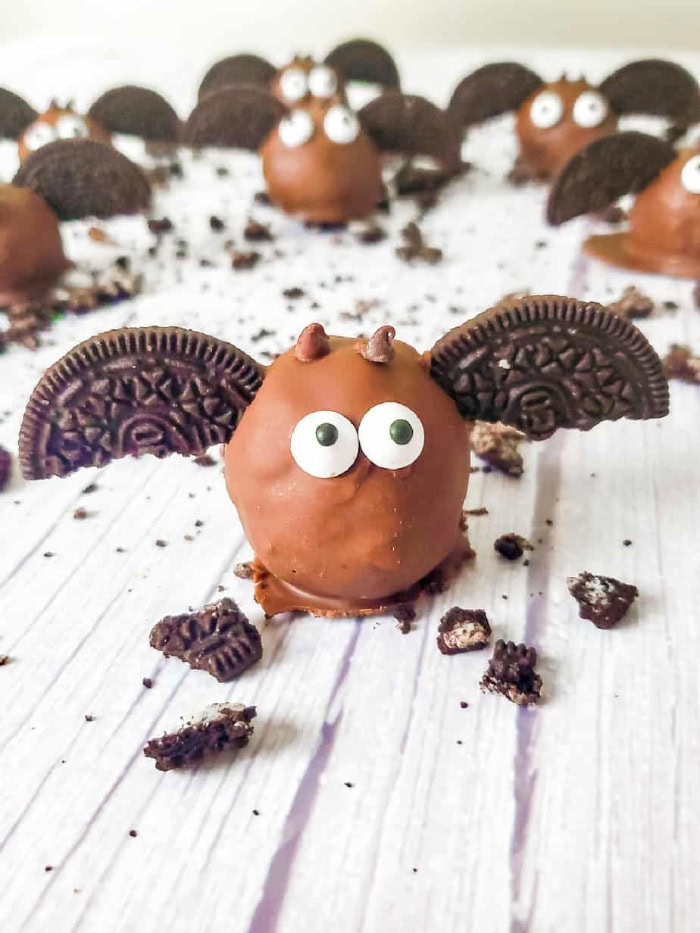 Several Chocolate Oreo bat truffles with cookie wings and candy eyes lined up on a white counter with oreo cookies crumb scatters.