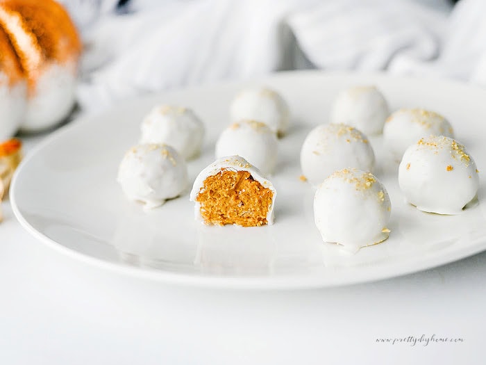 A plate of homemade pumpkin truffles topped with graham cracker cookie crumbs and served on a white plate with a fall pumpkin decoration.
