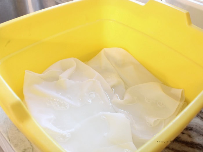 Vintage white damask tablecloth soaking in an OxiClean solution before washing.