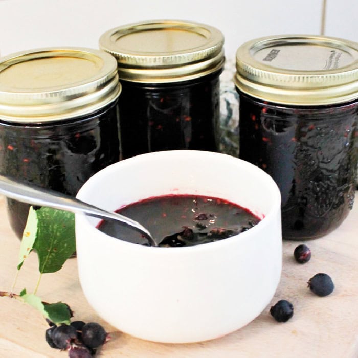 Homemade canning recipes with jars of berry preserves and a bowl of fresh fruit spread