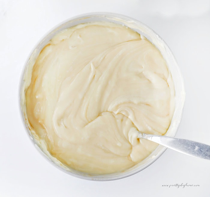 An overhead view of melted white chocolate Halloween fudge in a bowl with a spoon, ready to be spread into the prepared pan.