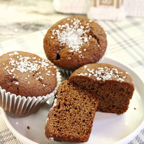 Cut gingerbread muffin showing the soft interior beside two muffins topped with sparkling sugar.