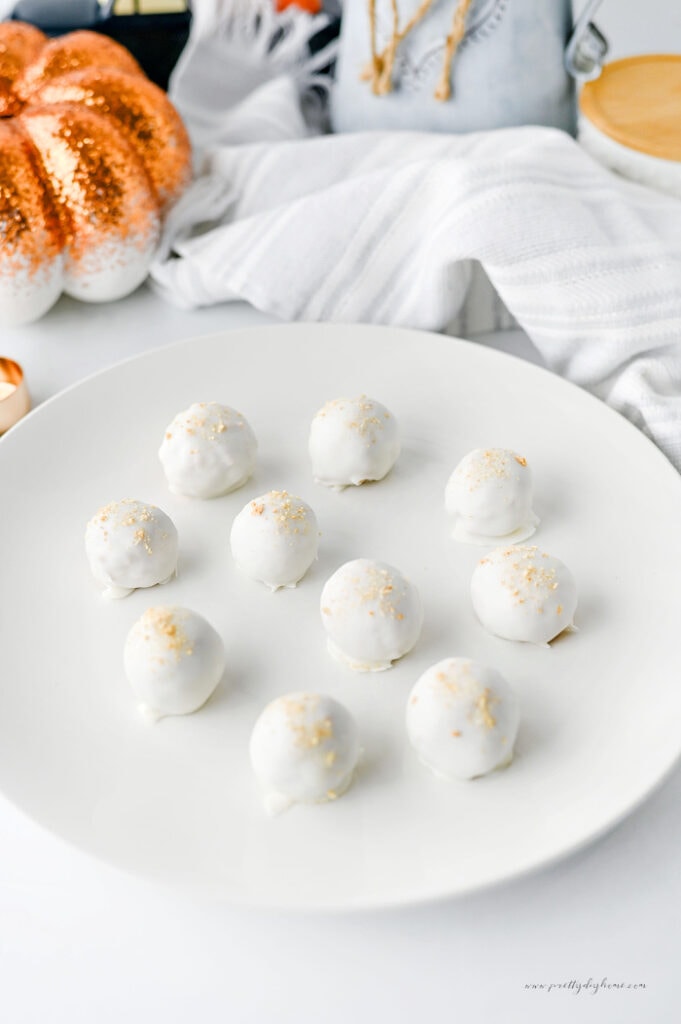 A plate of pumpkin truffles arranged on a white serving plate with a cozy fall pumpkin in the background.
