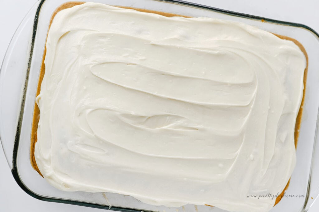 Cream cheese frosting spread over a cinnamon roll poke cake in a glass baking dish.