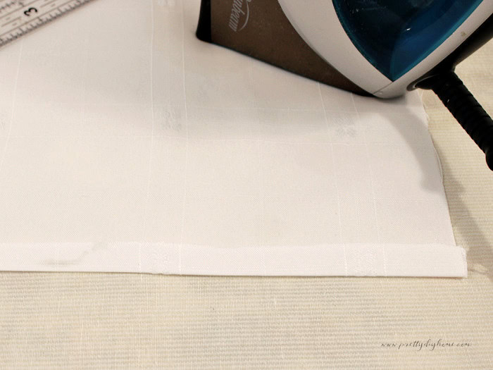 White damask fabric with a half-inch hem folded and pressed before forming the wider hem.