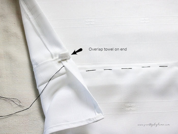 Black gathering stitches sewn across a damask ruffle with the first edge pinned over the back of the tea towel.