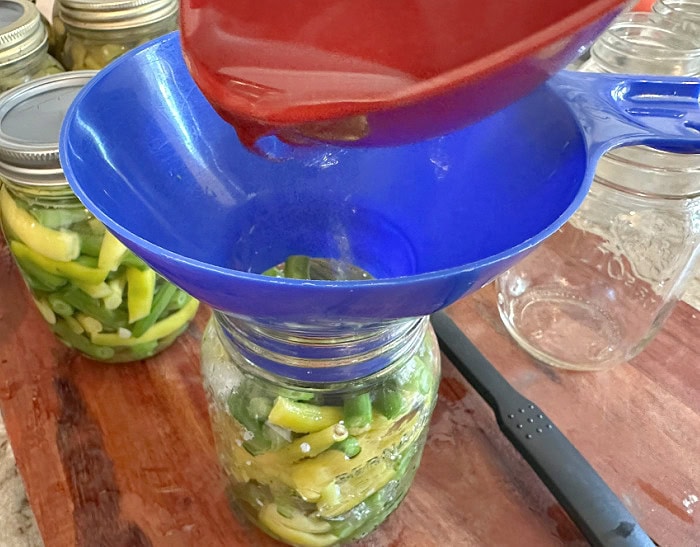Boiling water is being poured into a jar of green beans before pressure canning.