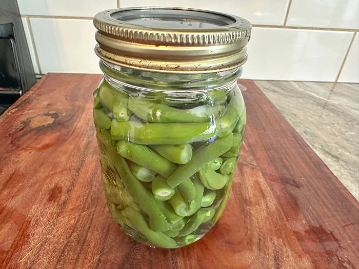 A canning lid and ring are being placed on a jar of green beans before pressure canning.