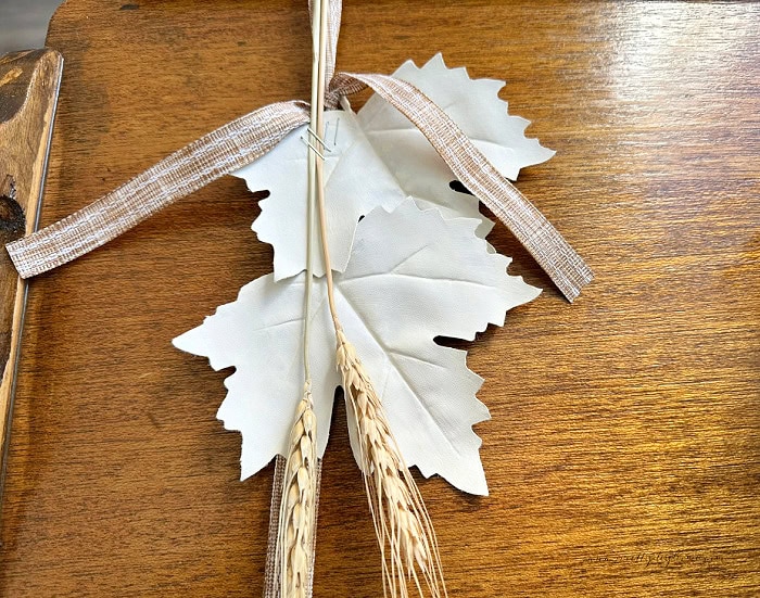 Cream painted fall leaves, wheat, and ribbon being attached to a vintage wood tray.