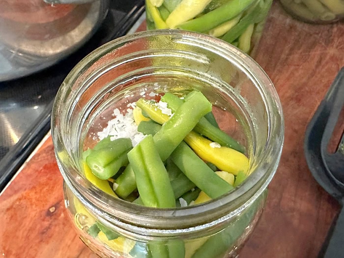 Pickling salt is being added to a jar of green beans before pressure canning.