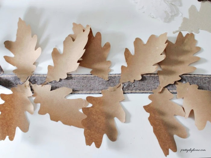 Brown paper bag oak leaves being attached along the fabric base while assembling the fall garland DIY.