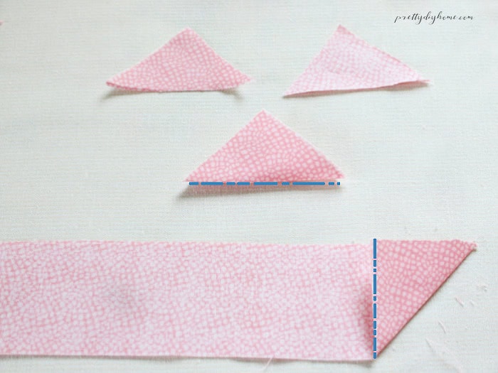 A strip of pink fabric marked with cut lines for making barn quilt triangles, with three finished fabric triangles shown above.