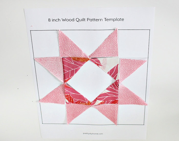 Pink and leaf fabric triangles arranged on a printed barn quilt pattern before attaching them to the wood block.