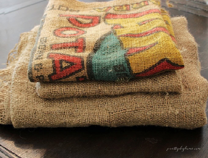A stack of clean natural burlap fabric with a colorful vintage printed burlap sack on top.