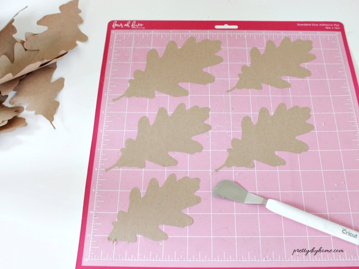 Different sizes of oak leaves cut from brown paper using the Cricut design file on a 12 by 12 cutting mat.