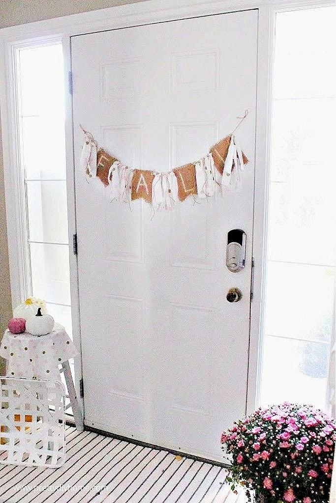 DIY fall burlap banner hanging on a white front door with pink mums and pumpkins.
