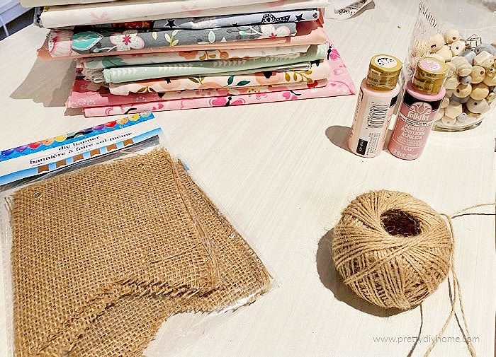 Supplies for a DIY fall burlap banner including burlap panels, twine, paint, fabric strips, and wooden beads